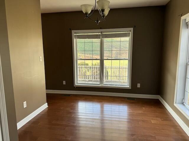 unfurnished dining area featuring a notable chandelier, a healthy amount of sunlight, and dark wood-type flooring