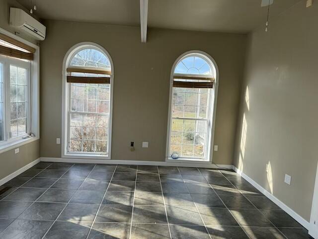 unfurnished room featuring a wall unit AC, a wealth of natural light, beamed ceiling, and dark tile patterned flooring