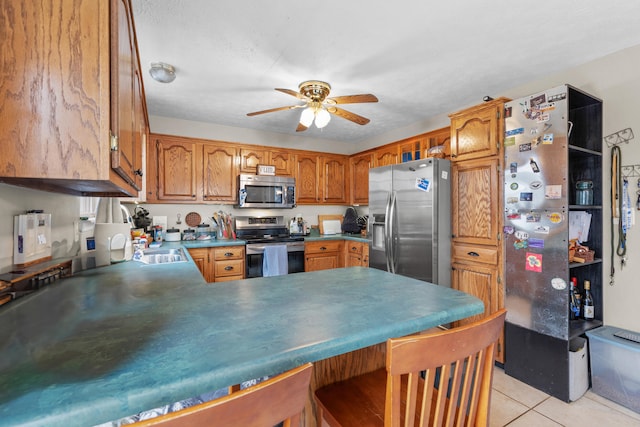 kitchen with kitchen peninsula, ceiling fan, light tile patterned flooring, and stainless steel appliances