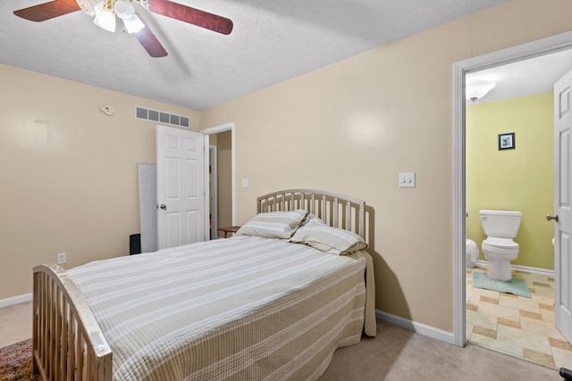 bedroom featuring a textured ceiling, light colored carpet, ensuite bath, and ceiling fan