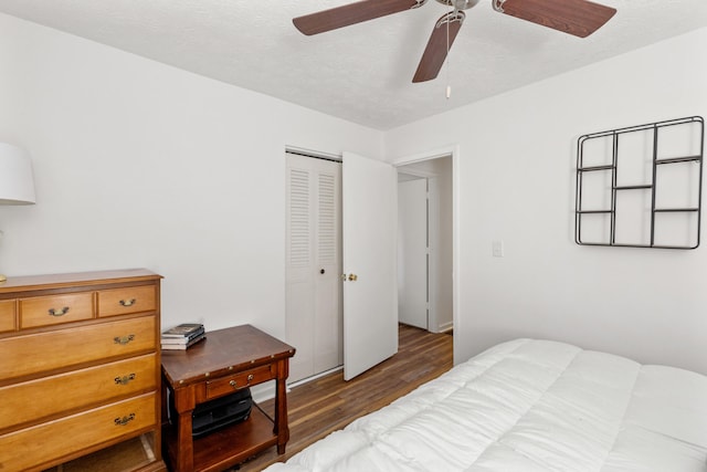 bedroom with a textured ceiling, ceiling fan, dark wood-type flooring, and a closet