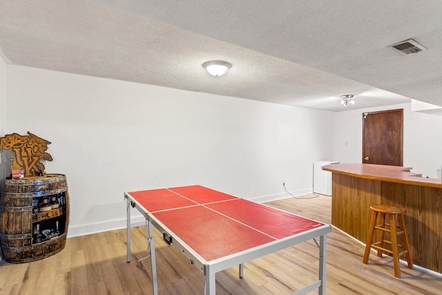 rec room with bar area, a textured ceiling, and light wood-type flooring