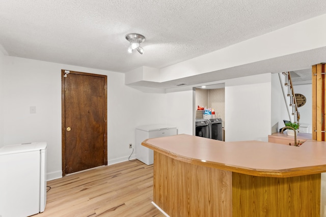 kitchen with washing machine and dryer, kitchen peninsula, a textured ceiling, fridge, and light wood-type flooring