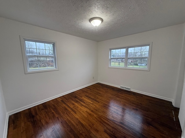 unfurnished room with a textured ceiling, plenty of natural light, and dark hardwood / wood-style floors