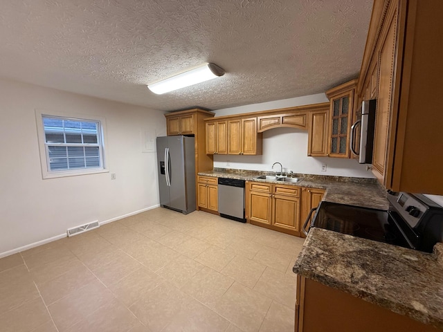 kitchen featuring a textured ceiling, stainless steel appliances, dark stone countertops, and sink