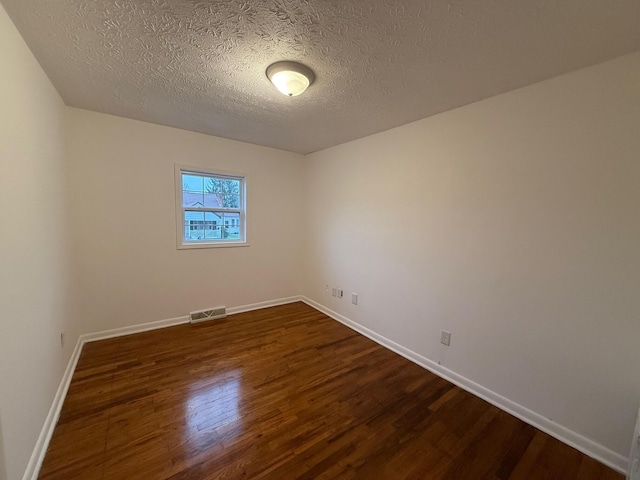 spare room with a textured ceiling and dark hardwood / wood-style floors