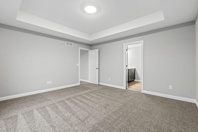 interior space with light carpet, ensuite bathroom, and a tray ceiling