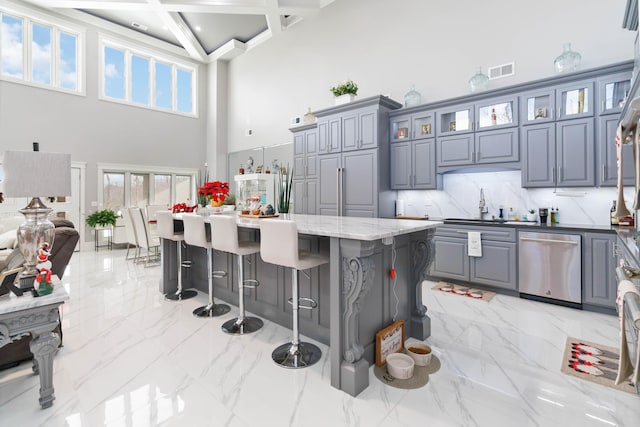 kitchen with a center island, sink, stainless steel dishwasher, light stone countertops, and a towering ceiling