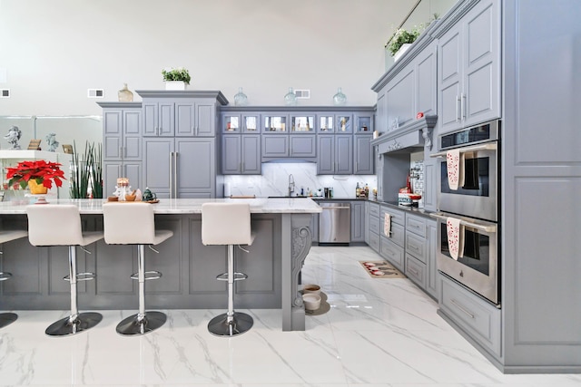 kitchen featuring gray cabinetry, light stone countertops, a kitchen island, a kitchen bar, and stainless steel appliances