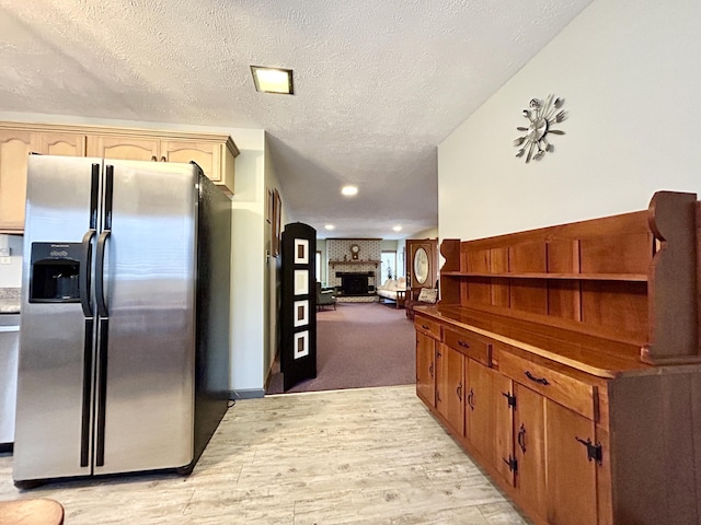 kitchen with a large fireplace, stainless steel fridge with ice dispenser, a textured ceiling, and light carpet