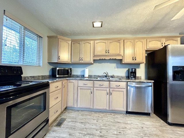 kitchen with light brown cabinetry, a textured ceiling, stainless steel appliances, ceiling fan, and sink