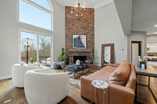 living room with a high ceiling, an inviting chandelier, a stone fireplace, hardwood / wood-style floors, and ornamental molding