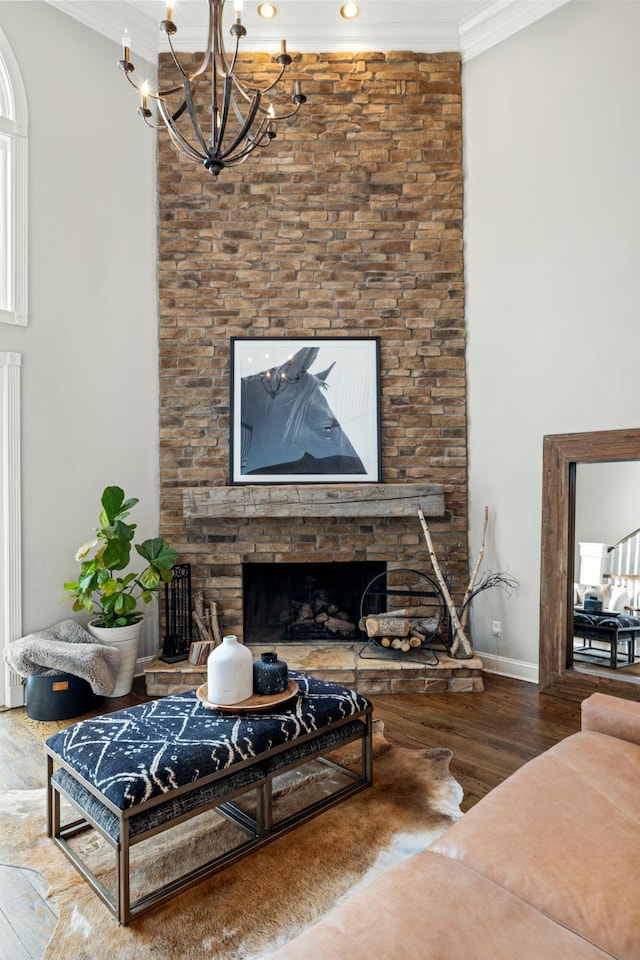 living room featuring hardwood / wood-style flooring, a stone fireplace, crown molding, and an inviting chandelier