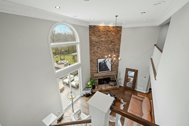 living room featuring a high ceiling, crown molding, a notable chandelier, a fireplace, and hardwood / wood-style floors