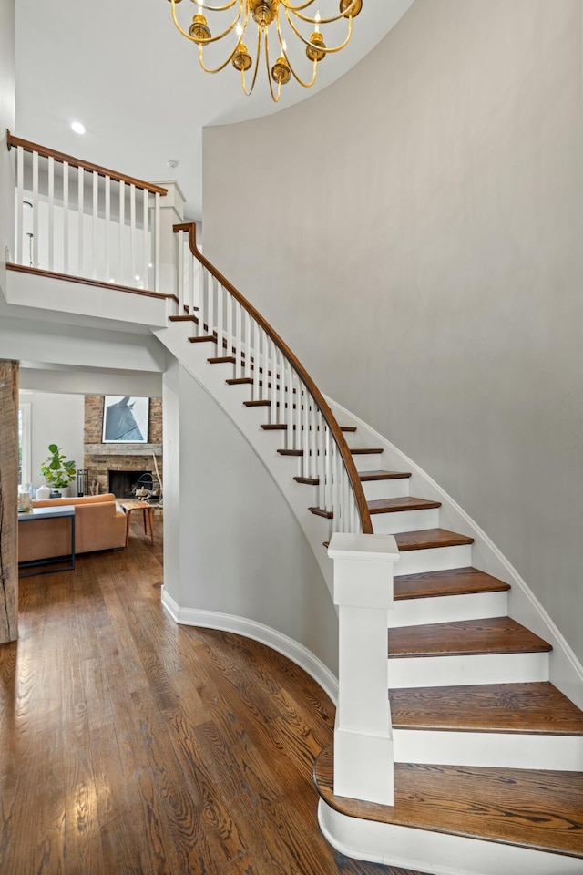 stairs with a chandelier, wood-type flooring, and a stone fireplace