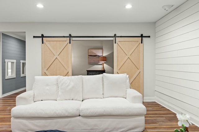 living room featuring a barn door, dark wood-type flooring, and wooden walls