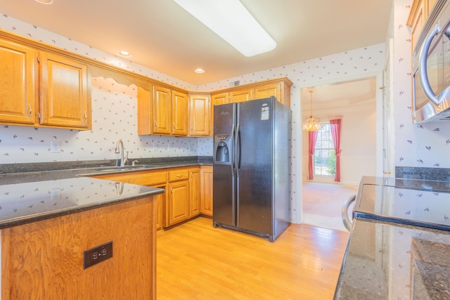 kitchen with light wood-type flooring, sink, black refrigerator with ice dispenser, and dark stone counters