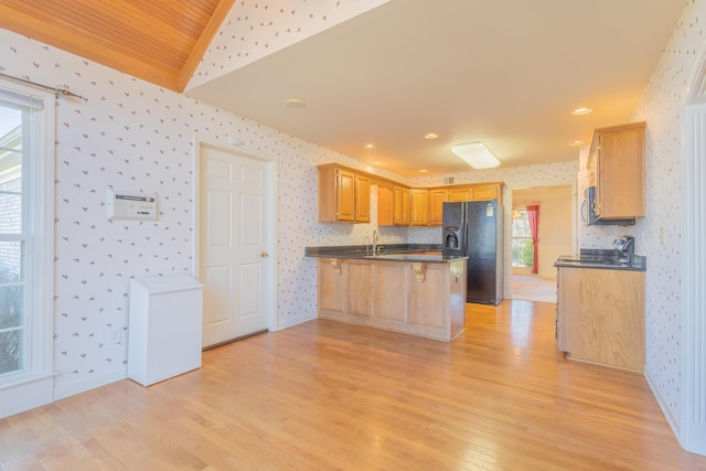 kitchen with kitchen peninsula, black fridge, sink, light hardwood / wood-style floors, and lofted ceiling