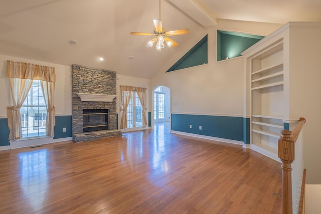 unfurnished living room with beam ceiling, ceiling fan, a stone fireplace, high vaulted ceiling, and hardwood / wood-style flooring