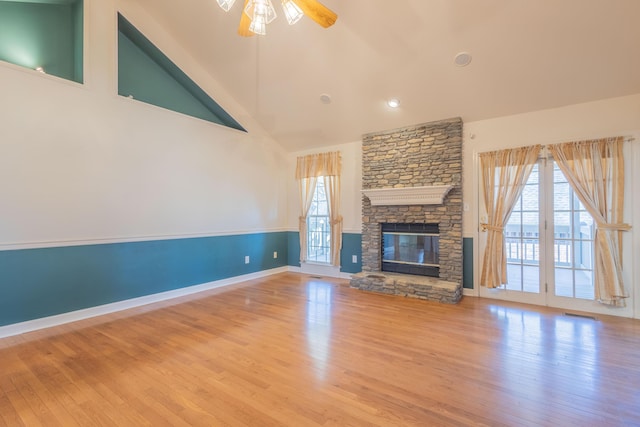 unfurnished living room with ceiling fan, a stone fireplace, light wood-type flooring, and high vaulted ceiling