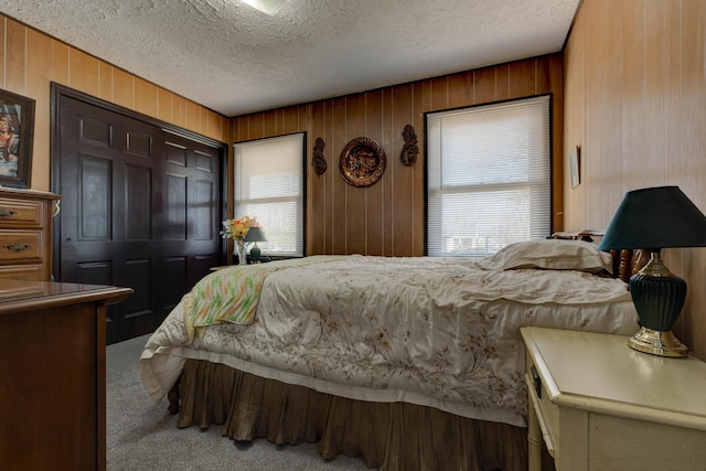 carpeted bedroom with a textured ceiling, a closet, and wooden walls