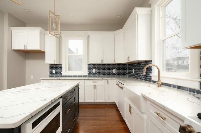 kitchen featuring light stone countertops, white cabinetry, sink, and pendant lighting