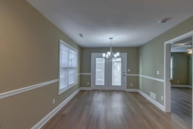 unfurnished dining area with ceiling fan with notable chandelier and light hardwood / wood-style floors