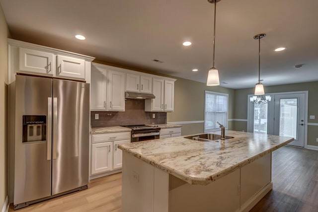 kitchen with a center island with sink, sink, appliances with stainless steel finishes, decorative light fixtures, and white cabinetry