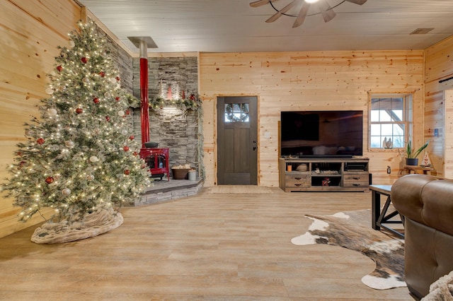 living room with hardwood / wood-style floors, a wood stove, ceiling fan, and wooden walls