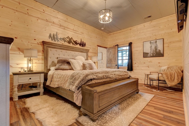 bedroom with light wood-type flooring, an inviting chandelier, and wood walls