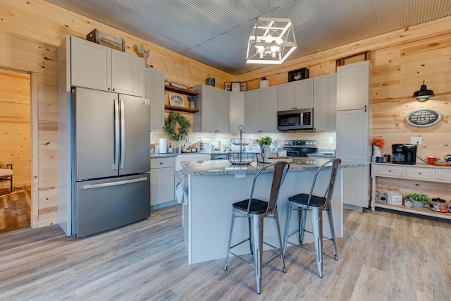 kitchen with a center island, wooden walls, a breakfast bar area, light hardwood / wood-style floors, and stainless steel appliances