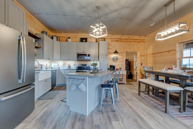 kitchen featuring stainless steel appliances, a kitchen island, hanging light fixtures, and light hardwood / wood-style flooring