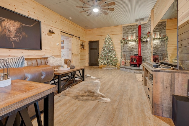 living room featuring a barn door, light hardwood / wood-style flooring, a wood stove, and wood walls