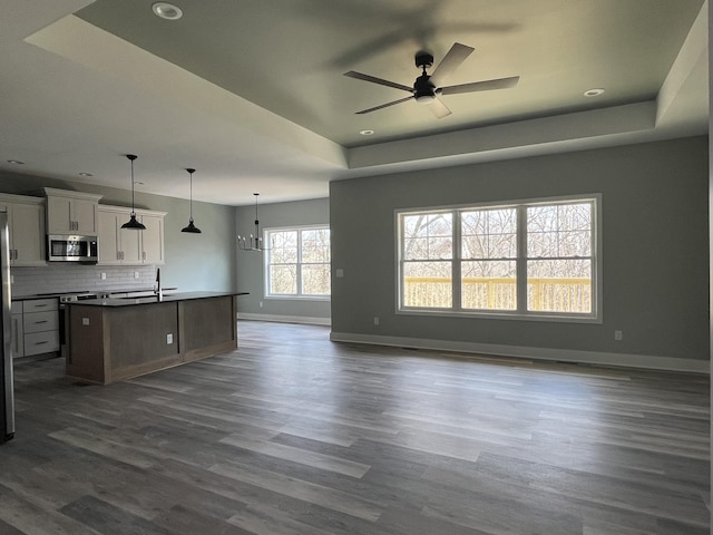 kitchen featuring baseboards, open floor plan, a tray ceiling, stainless steel microwave, and dark wood finished floors