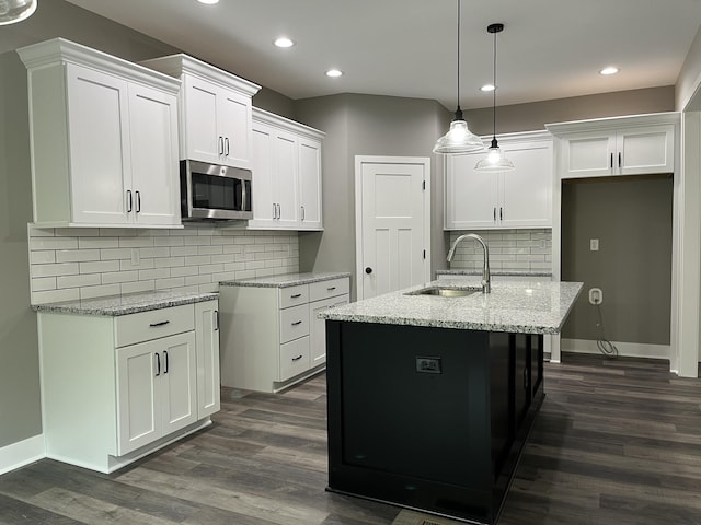 kitchen featuring white cabinetry, sink, light stone counters, and a center island with sink