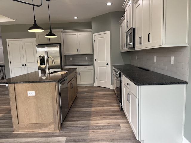 kitchen featuring a kitchen island with sink, stainless steel appliances, a sink, dark stone counters, and dark wood finished floors