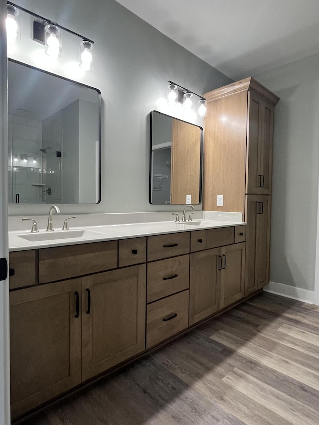 full bath featuring a sink, double vanity, tiled shower, and wood finished floors