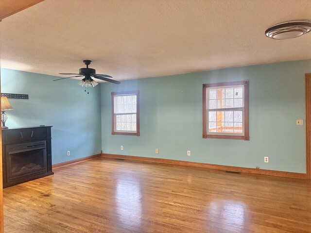 unfurnished living room featuring a textured ceiling, light wood-type flooring, and ceiling fan