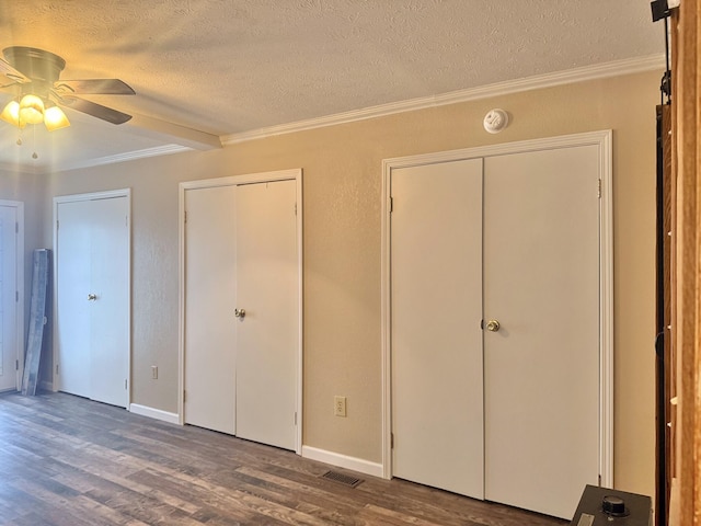 unfurnished bedroom featuring two closets, crown molding, dark hardwood / wood-style floors, ceiling fan, and a textured ceiling