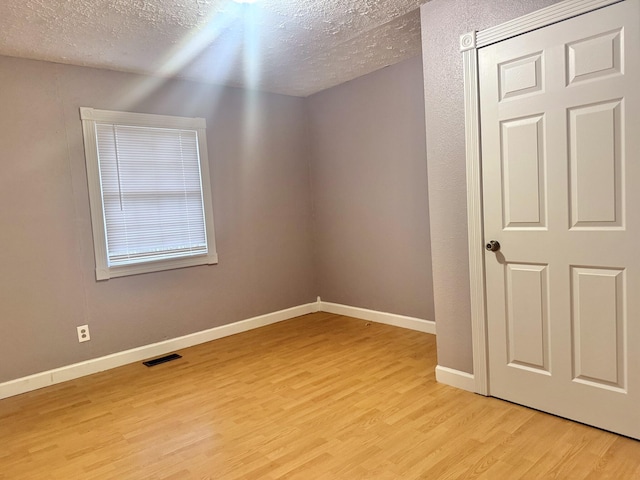 empty room with a textured ceiling and light hardwood / wood-style flooring