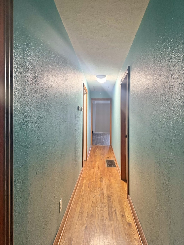 hall with light hardwood / wood-style floors and a textured ceiling