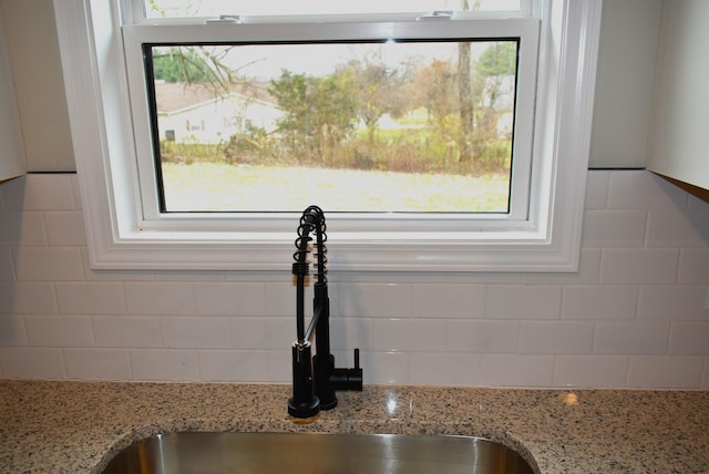 room details featuring decorative backsplash, light stone countertops, and sink