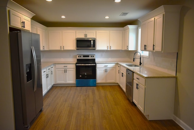 kitchen with sink, light hardwood / wood-style flooring, appliances with stainless steel finishes, light stone counters, and white cabinetry