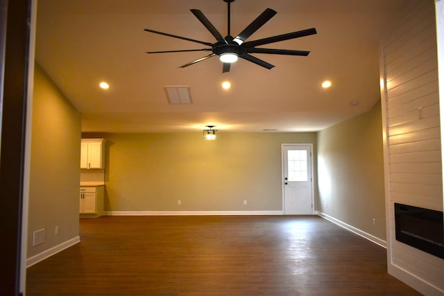 unfurnished living room featuring ceiling fan, a large fireplace, and dark wood-type flooring