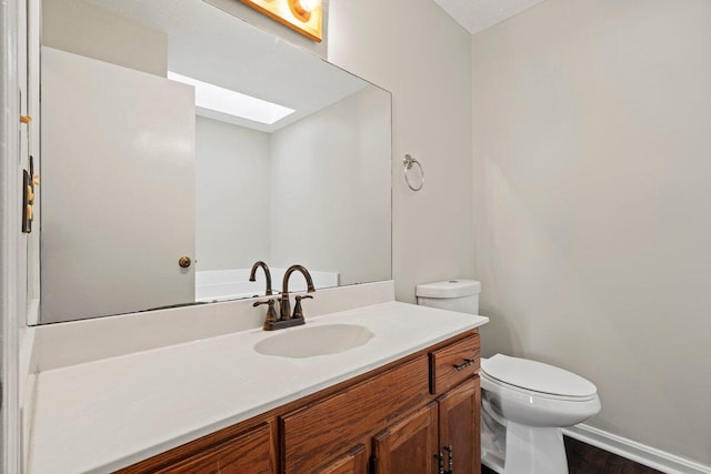 bathroom featuring a skylight, toilet, vanity, and baseboards