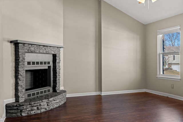 unfurnished living room with a stone fireplace, baseboards, and dark wood-style flooring