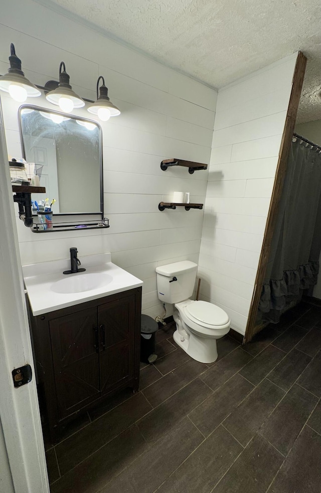 bathroom featuring vanity, toilet, a textured ceiling, and wooden walls