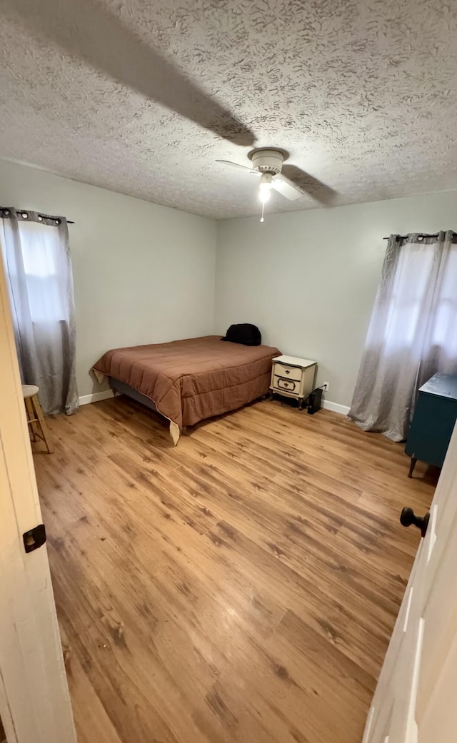 bedroom with ceiling fan, light hardwood / wood-style flooring, and a textured ceiling