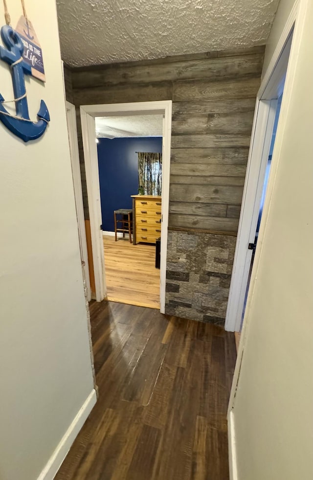 hall featuring wooden walls, dark wood-type flooring, and a textured ceiling