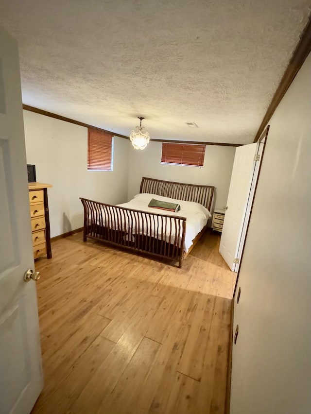 bedroom featuring light hardwood / wood-style flooring, a textured ceiling, and ornamental molding